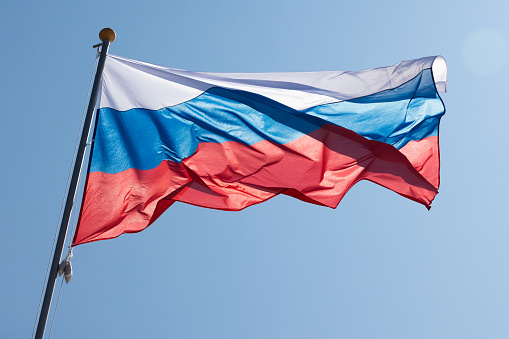 The national flag of Russia, also known as the State Flag of the Russian Federation is under bright blue sky on a sunny day