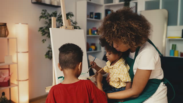 African American mom helping little sons paint a picture on canvas, family hobby