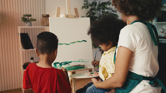 Happy black family painting at easel stand together, little boy mixing colors