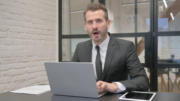 istock Shocked Middle Aged Businessman Looking at Camera while Working on Laptop 2140112673