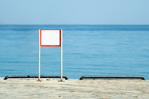 Blank warning sign by the sea on a sunny clear summer day