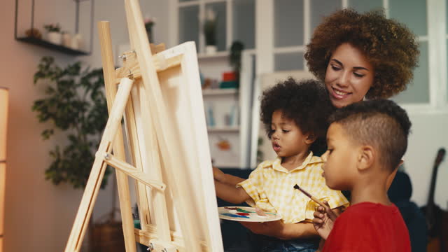 Smiling mother helping little sons paint a picture, children's development, art