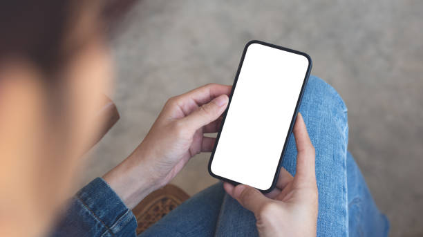 istock Cell phone white screen mockup, woman's hands holding mobile phone with blank screen on thigh and, overhead view. space for advertise, social media marketing design 2140123535