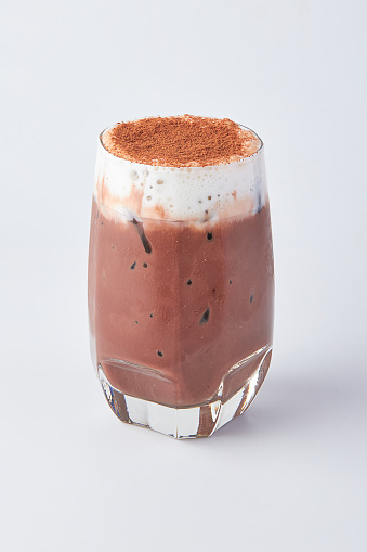 Iced Chocolate with milk foam topped with chocolate powder served in a clear glass isolated on white background.