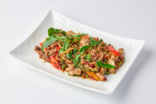 Stir fried spicy Frog leg with vegetables and herbs (chilli, galangal, kaffir lime leaves and basil) served on white plate isolated on white background.