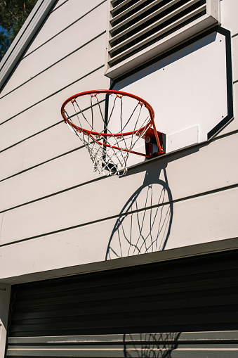 Red basketball hoop attached to a wall with shadow pattern on a sunny day.