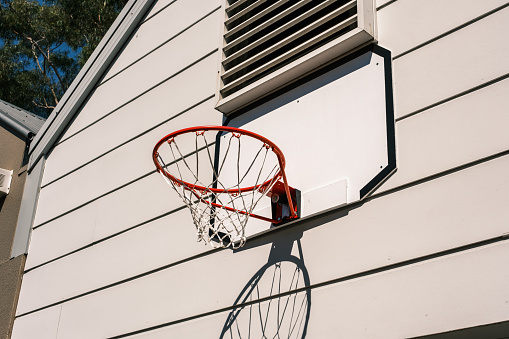 Red basketball hoop attached to a wall with shadow pattern on a sunny day.