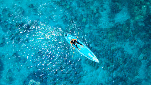 vista aérea de una mujer navegando en kayak en el mar azul y aguas cristalinas. se pueden ver corales bajo el mar. - canoa en la playa tropical fotografías e imágenes de stock