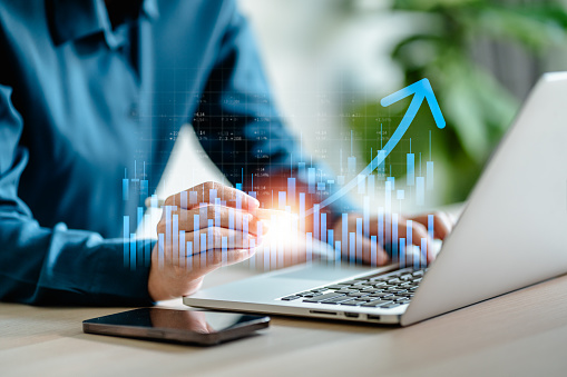 Businesswomen analyze on laptop the stock market with a digital virtual chart,  trend upside business market growth, investments and financial concept.
