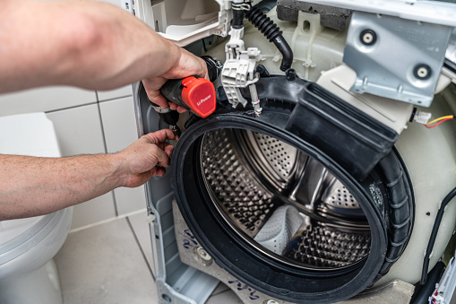 A repairman removes a damaged rubber gasket on the drum of a washing machine.