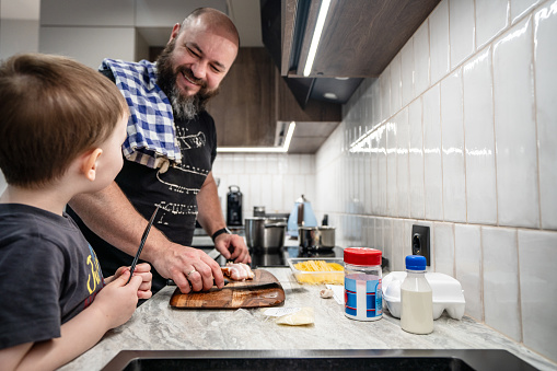 Joyful father and son are cooking together at the kitchen
