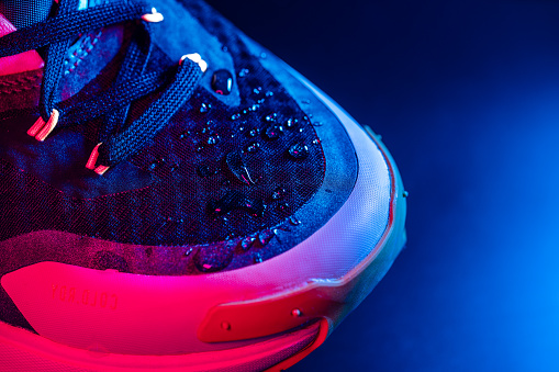 Waterproof footwear. Drops of water on the trail running shoes. Neon coloured lighting