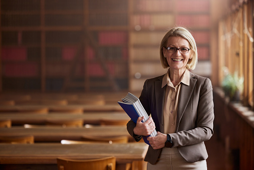 Portrait of happy senior lawyer standing in library and looking at camera.
