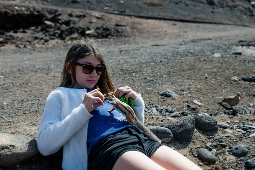 Beautiful young girl feeding a wild squirrel in the mountains of Fuerteventura.