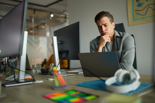 Displeased male programmer reading problematic codes on a computer in the office.