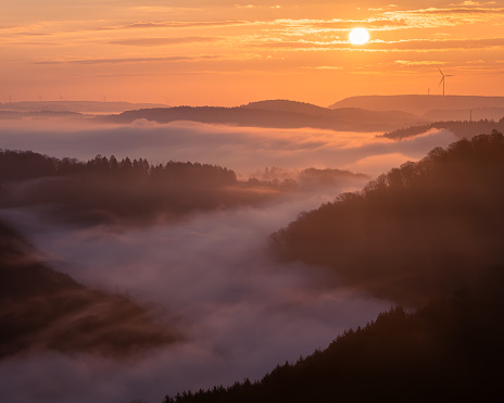 A beautiful view of the misty hills with a distant wind turbine at sunrise