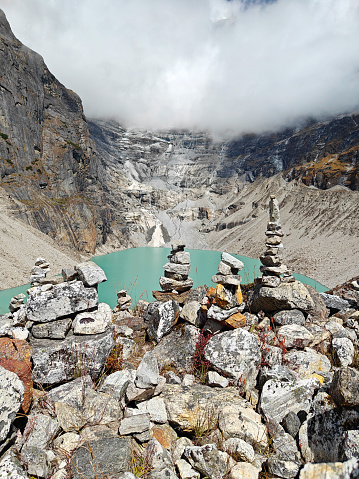 Stone cairns overlooking a turquoise glacier lake surrounded by rugged mountains.