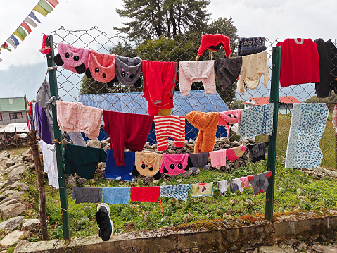 Colorful clothes hanging on a wire fence with prayer flags and trees in the background.