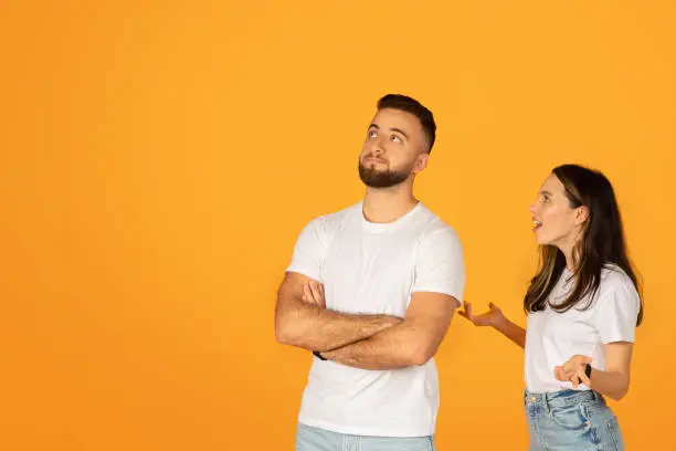 Skeptical man with crossed arms looking unconvinced beside a talking woman, both in white t-shirts against an orange background, depicting a potential disagreement or debate