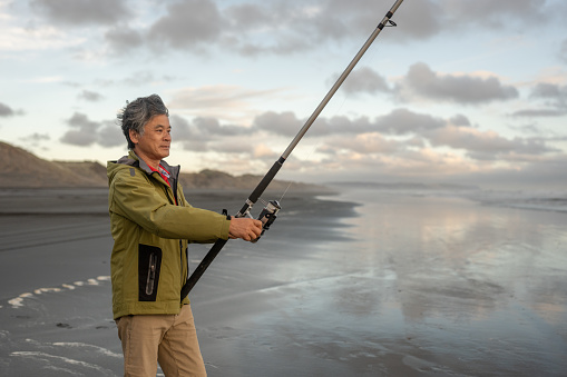 An elderly Asian man fishing on a beach