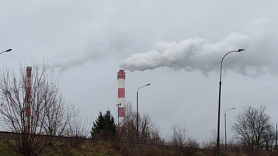 Thermal power plant smokes against the backdrop of a cityscape on the cloudy day