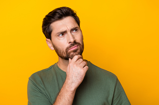 Photo of thoughtful doubtful guy dressed green t-shirt hand chin looking empty space isolated yellow color background.