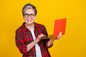 Portrait of positive grandmother toothy smile hold microsoft apple laptop empty space isolated on yellow color background