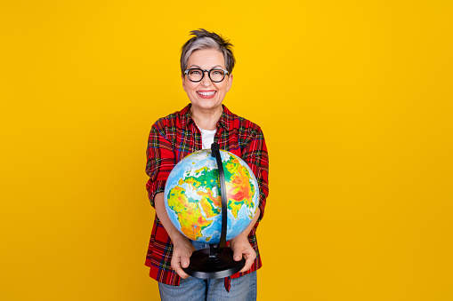 Photo of cheerful aged person toothy smile arms hold world globe empty space isolated on yellow color background.