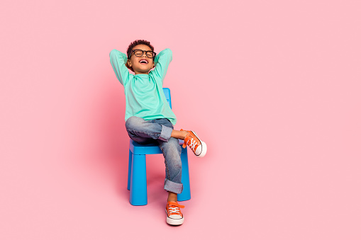 Full length photo of adorable little boy sit chair hands behind head specs wear trendy aquamarine garment isolated on pink color background.