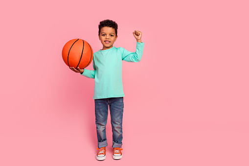 Full size photo of charming small boy hold basketball ball raise fist wear trendy aquamarine outfit isolated on pink color background.