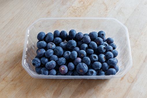 Top down shot of blueberry in plastic container on wooden surface.