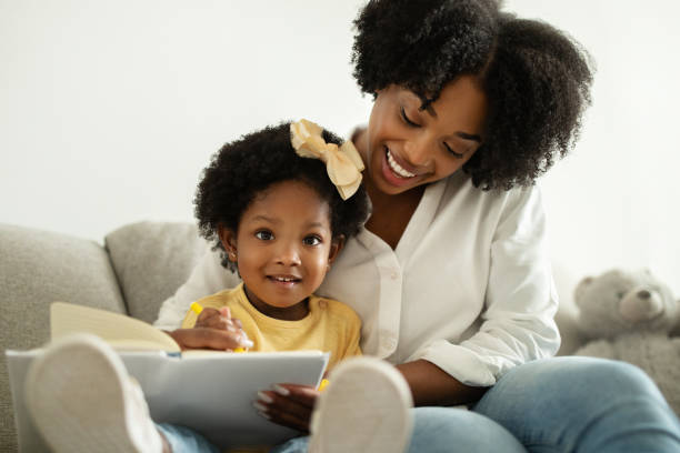istock Pretty Black Mommy Reading Book With Her Cute Infant Daughter 2140404330