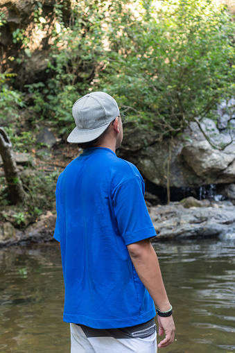 A young man in a blue shirt gazing at a forest waterfall.