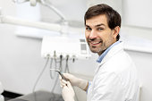 Portrait of male dentist posing with at workplace in dentistry clinic office, smiling at camera, ready for invite patient