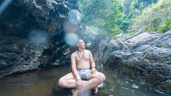 A person in a meditative pose at the base of a waterfall, embracing nature's serenity.