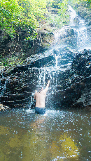 Person in a waterfall, arm raised, back to the camera.