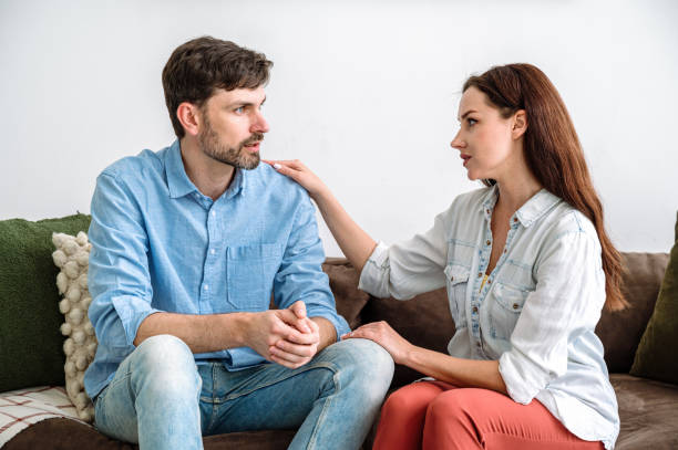 istock Young husband sitting on sofa, talking about problems, wife listening carefully 2140420653