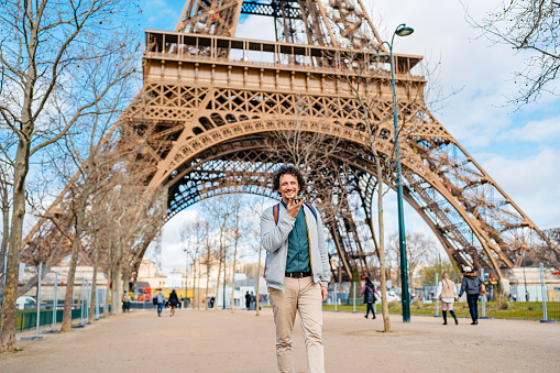Handsome young man sending a voice message on his smart phone in front of an Eiffel Tower in Paris in France.