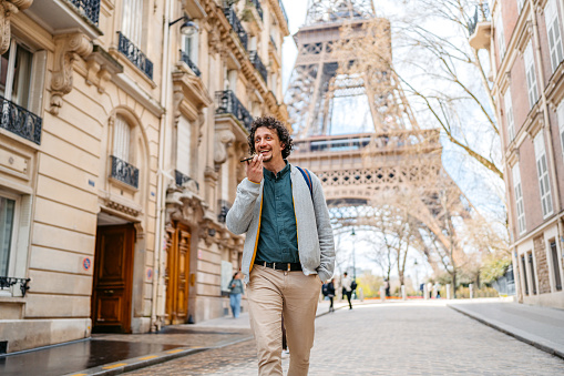 Handsome young man sending a voice message on his smart phone in front of an Eiffel Tower in Paris in France.