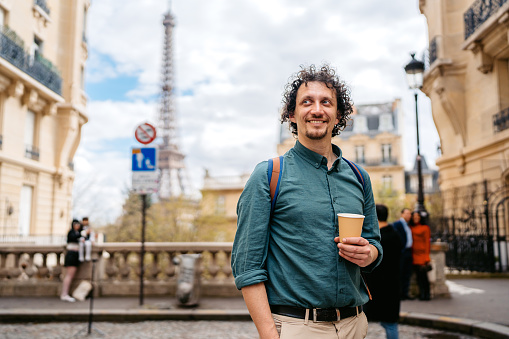 Handsome young man drinking coffee to go near Eiffel Tower in Paris in France.