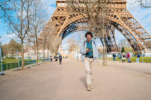 Handsome young man using his smart phone in front of an Eiffel Tower from the street in Paris in France.