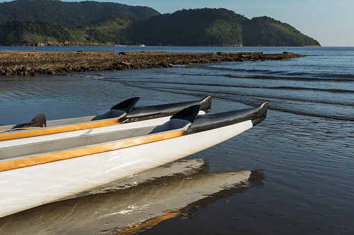 Hawaiian canoe on the beach close to the sea in the region of water channel nº6. Reflection in the water mirror. City of Santos, Brazil.