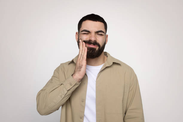 istock Man with a beard winces in discomfort, touching his cheek with a hand 2140480334