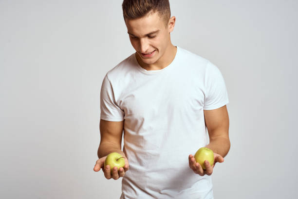 istock a guy with apples in his hands on a light background in a white t-shirt gesticulate with his hands smile 2140500728