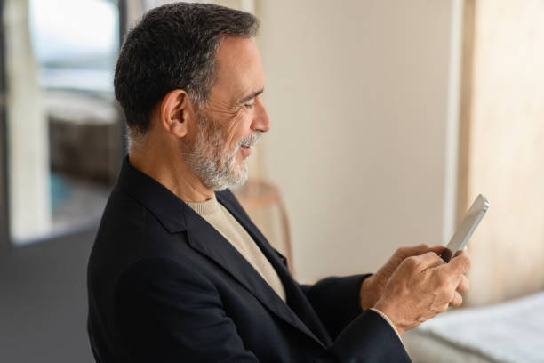 vista do perfil de um homem sênior alegre em uma roupa casual inteligente usando um smartphone - smart casual side view one person success - fotografias e filmes do acervo