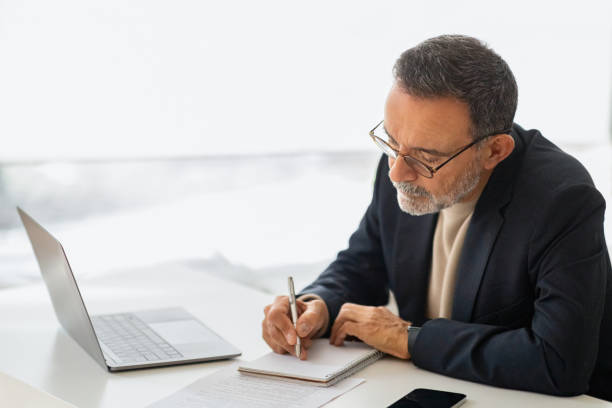 istock A thoughtful, mature businessman in a smart suit takes notes with a pen in a notebook 2140503387