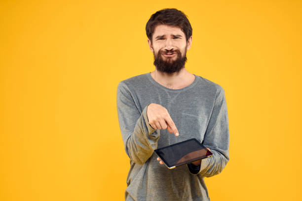 istock Emotional man with tablet in hands technology internet device lifestyle yellow background 2140523044