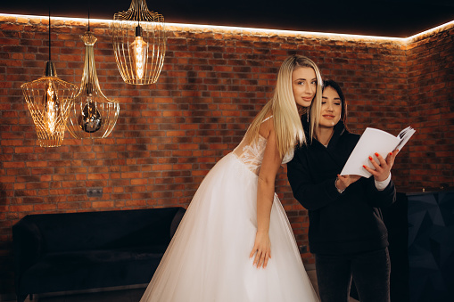 a consultant in a wedding salon shows a woman a catalog of wedding dresses
