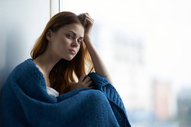 istock woman sitting on a windowsill covered with a blanket rest pensive view 2140620081