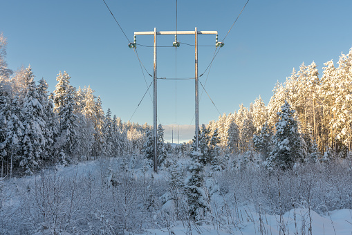 Sunny winter view of snow covered powerlines and pylons crossing a forest in the swedish countryside